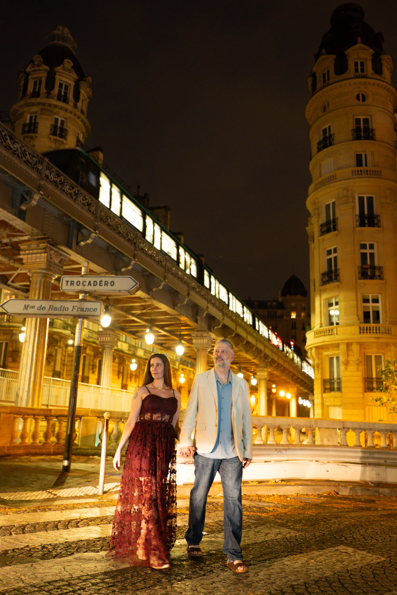 A couple photographed together beside the illuminated Paris Métro at night