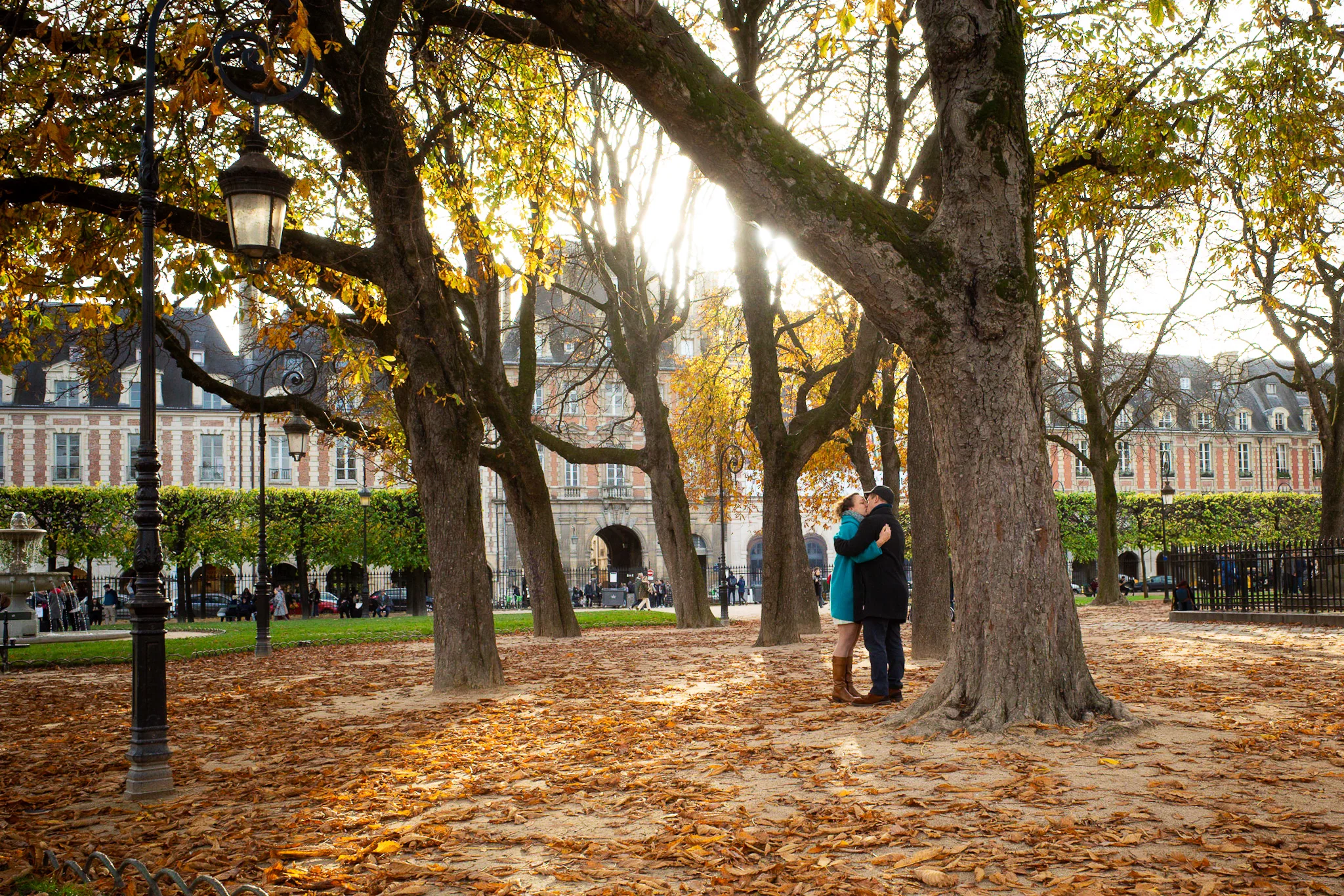 Couple beneath golden autumn trees in Place des Vosges, Paris