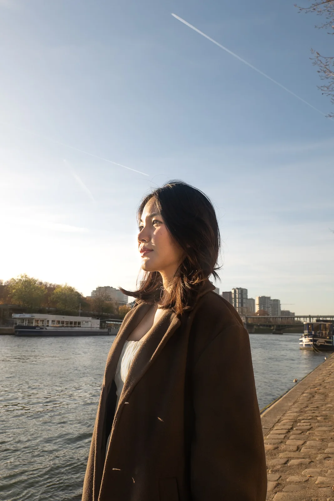 Woman in a brown coat beside the Seine in warm autumn morning light