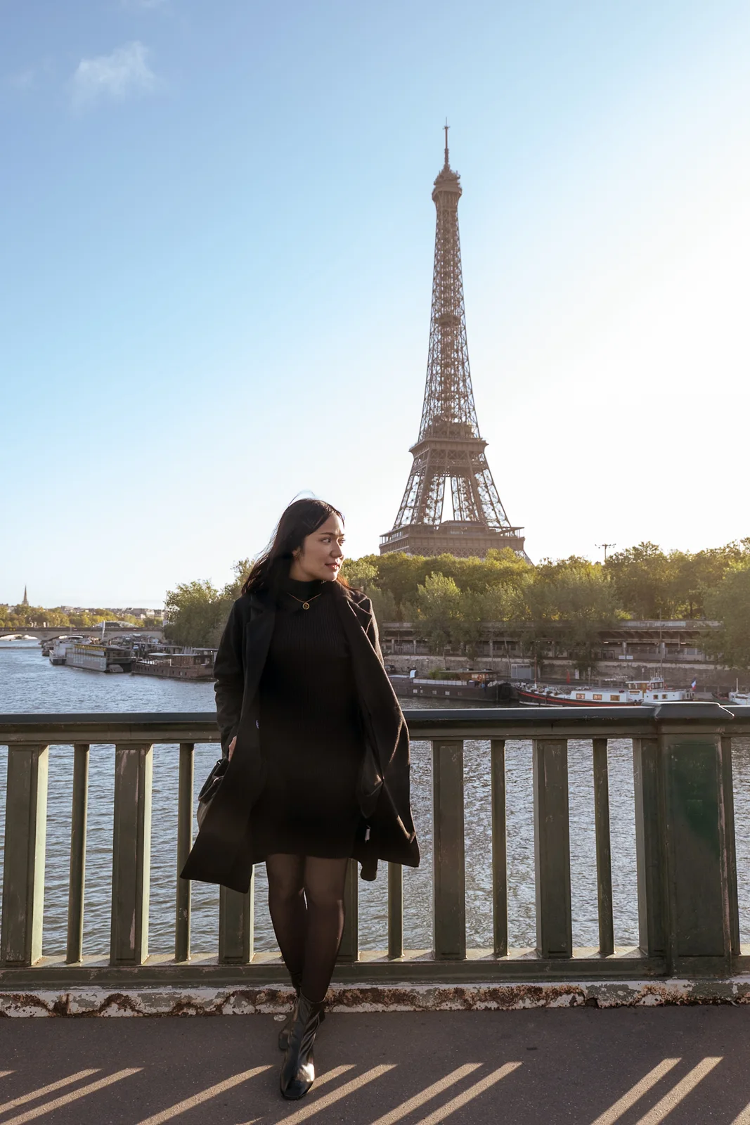 Woman standing on a Paris bridge with the Eiffel Tower in soft morning light
